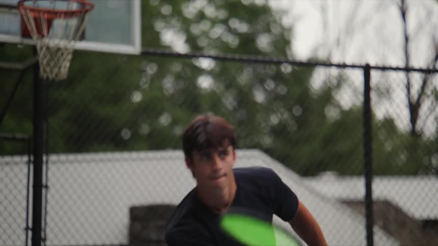 Young man running back and forth on a court playing tennis with a racket