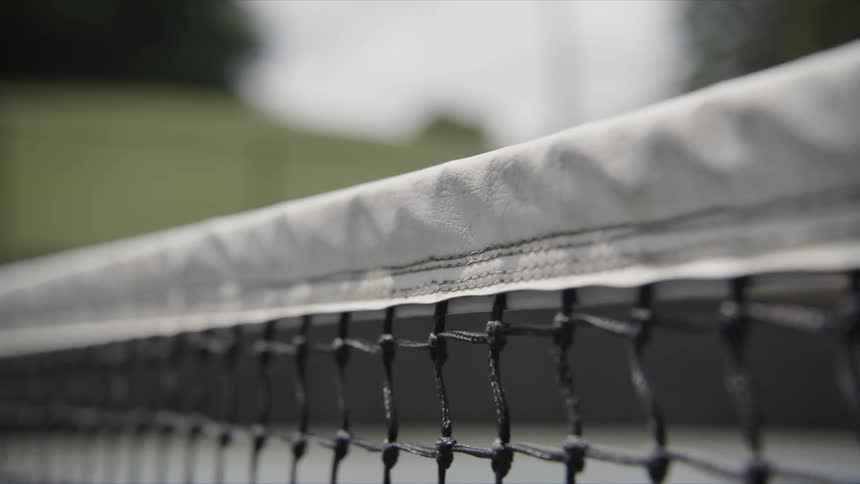 Close up of a tennis net on an open court and a person in the background running