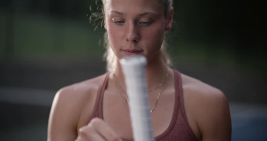 Young blonde woman wrapping her tennis racket