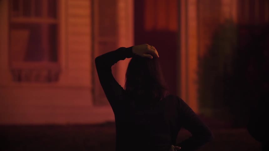 A woman holds her hand on her head while lights flash outside