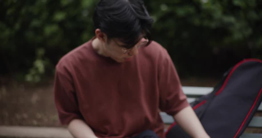 Young man sitting down putting away his cell phone and picking up his tennis racket and standing up