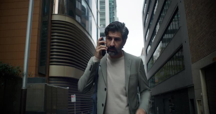 An older man answers his smartphone while he walks through a city downtown area
