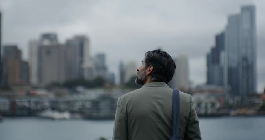 A man with a beard stands outside of a city looking at it