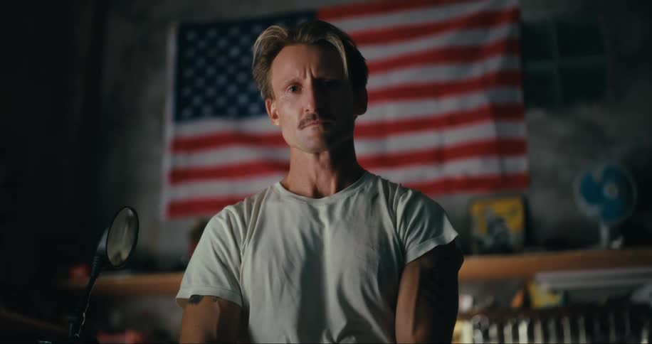Portrait of a blond man with a mustache in a garage with the flag in the background