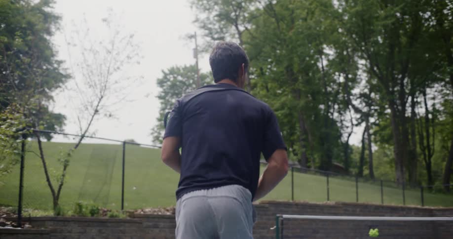 A male plays tennis on an outdoor court