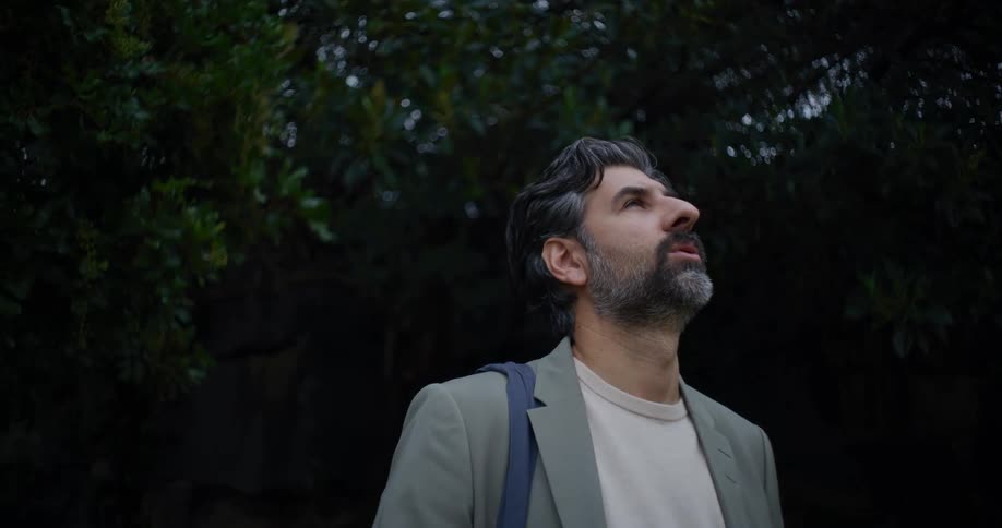Man in formal wear looking up with trees in the background