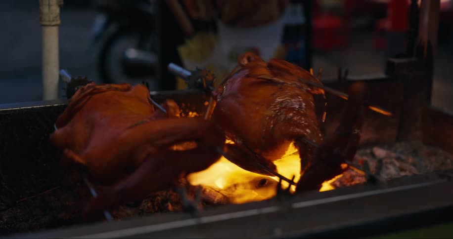Two roasted ducks rotate over open flames on a street vendors stall