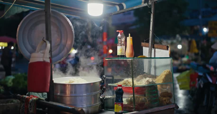 Cooking steaming food at a stall next to a busy street at night
