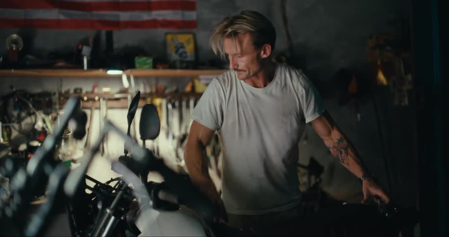 A man fixes a motorcycle on a workshop under an american flag