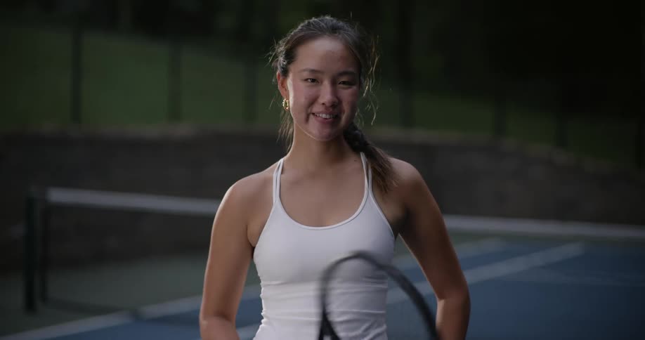 Teenage girl smiles while twirling her tennis racket