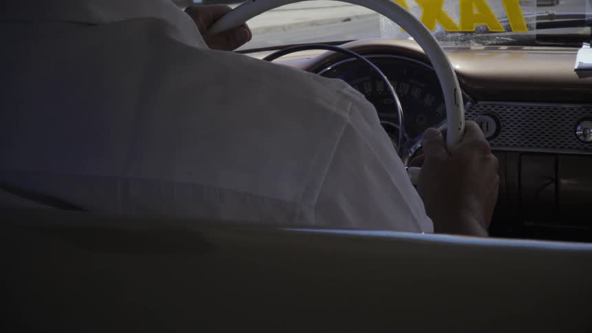 A cab driving is gripping the wheel as he drives during the day