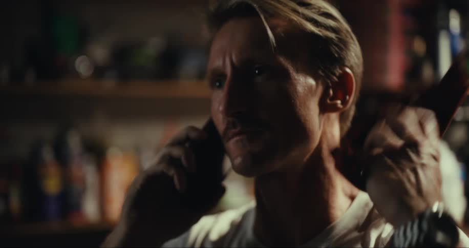 A man with a mustache talks on a smartphone while in a garage