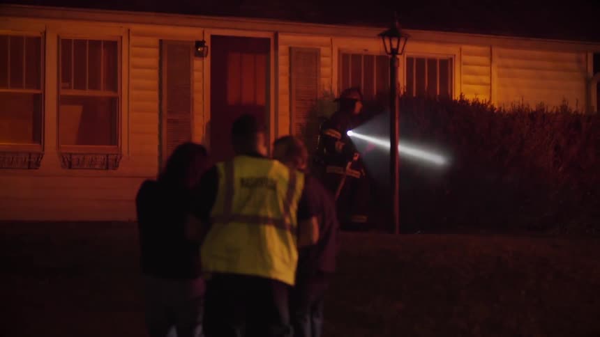 A fireman exits a house while shining a flashlight