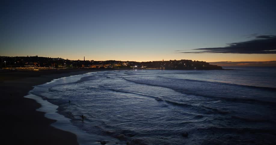 A beach in the morning with the sky still dark and some surfers entering the water which has some small waves