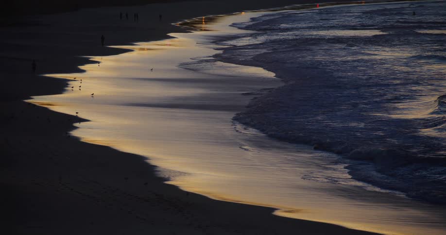 Waves gently rolling on the sandy shoreline at sunset