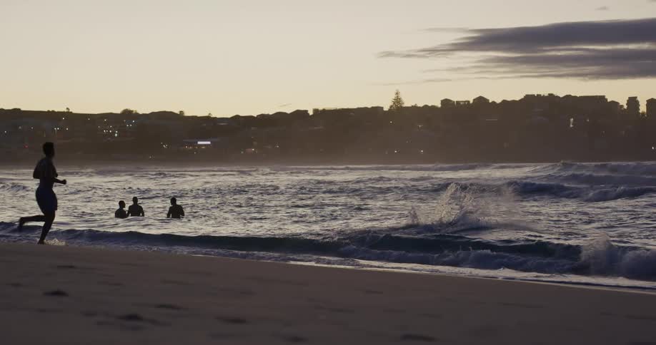 Silhouette of people enjoying a beach next to a coastal city at sunset
