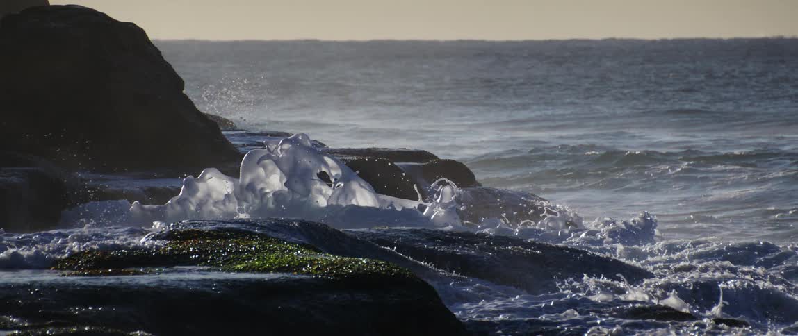 Ocean waves crash over large rocks in slow motion