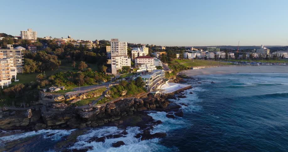 Waves crash against a rocky coast near a large city