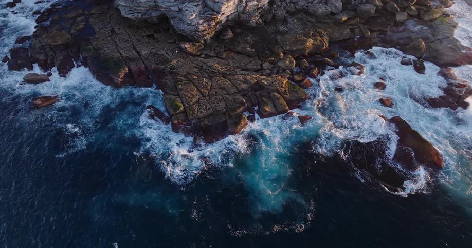 Aerial view of a rocky coastline surrounded by blue sea and crashing waves