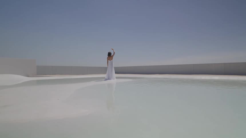 Woman in long white dress with hand up standing in the center of a salt lake landscape