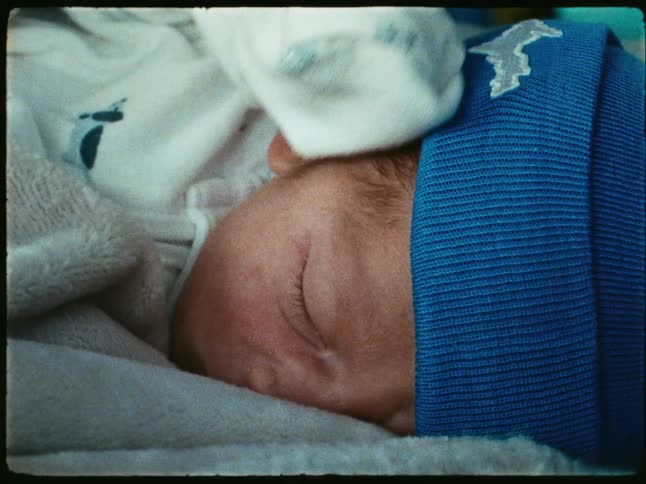 Young baby bundled into pajamas and a knit hat lies with its eyes closed