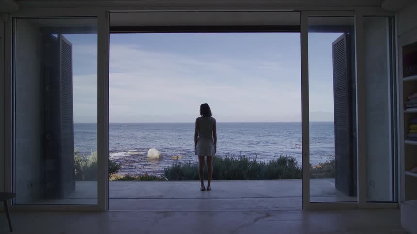 A woman shown from behind walks through a glass doorway onto the beach