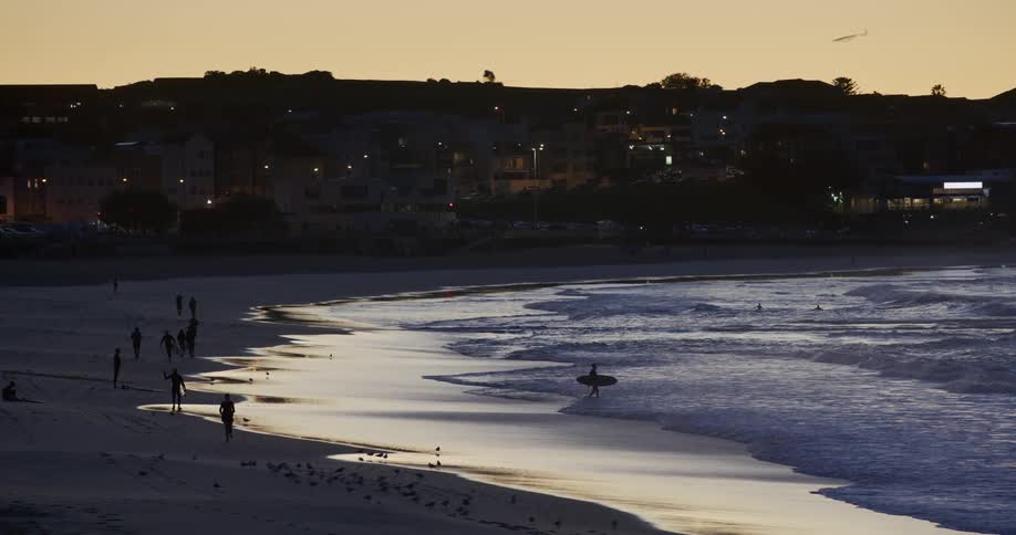 People on the beach sand with surfers at sunrise