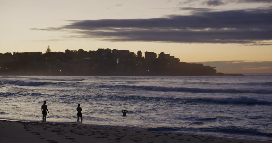 The silhouette of some people standing on a beach in the morning and in the background there is a city