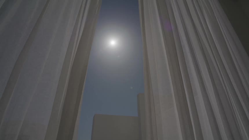 Sun seen through an opening between two white curtains