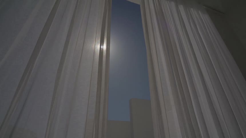 A breeze gently blows white window drapes