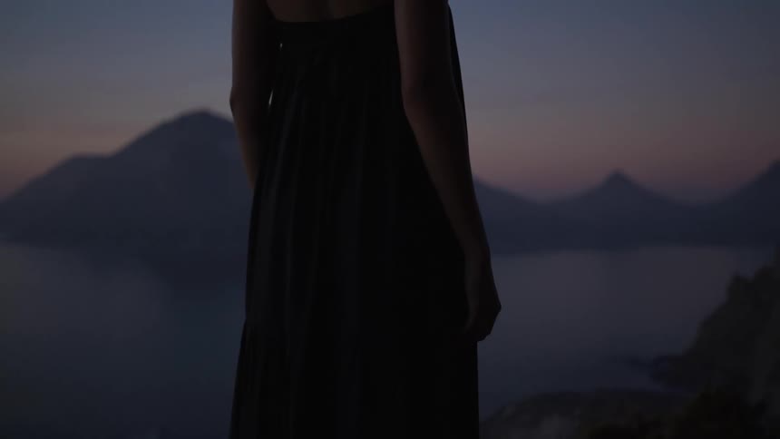 Woman in a long sleeveless dress by the sea on a morning with a purple sky