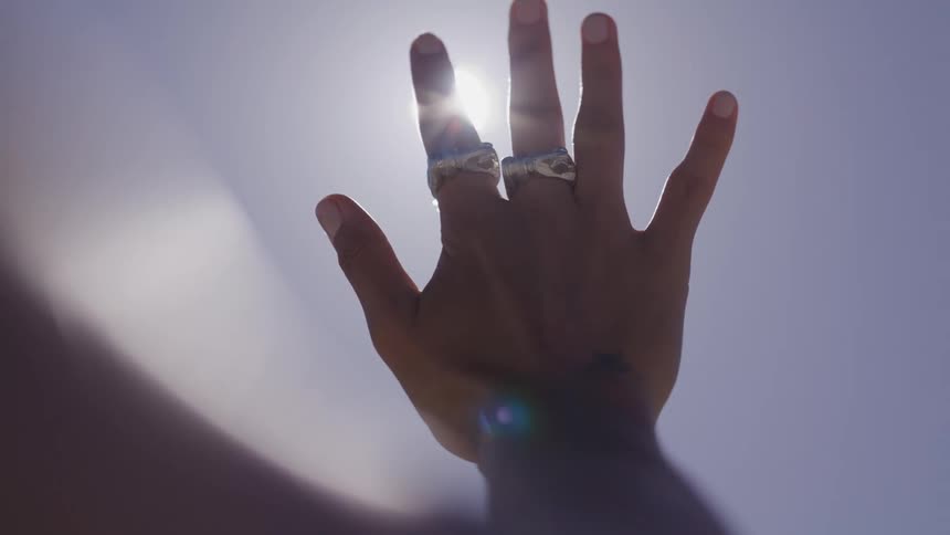 Womans hand with two rings pointing to the sky against the sunlight