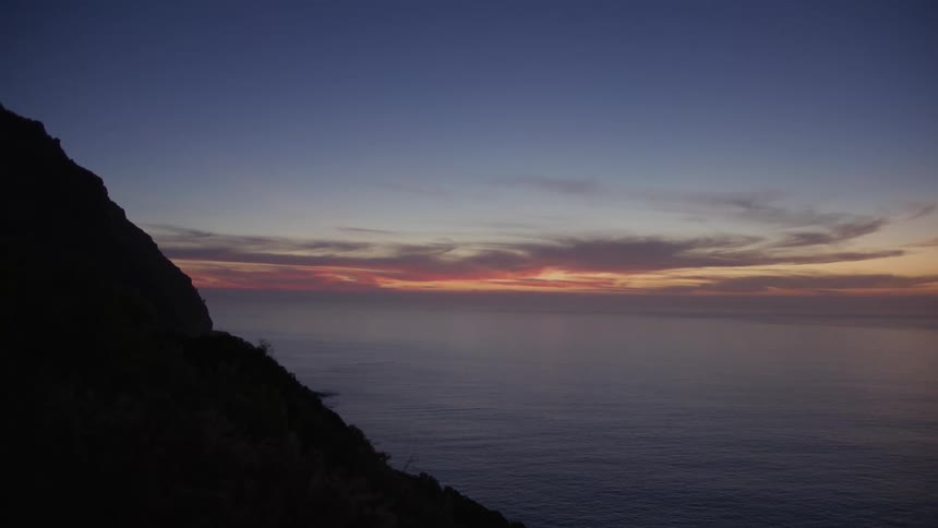 Ocean landscape with the silhouette of the rocky coast and a sky at dawn in shades of purple and red