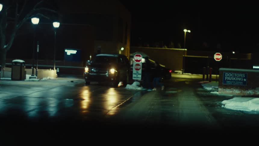 Entrance to a hospital with a car parked at night and two people walking