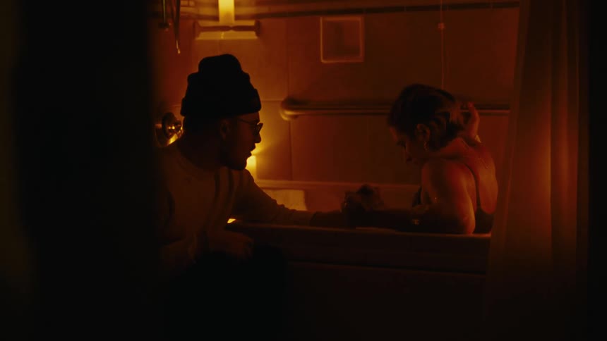 Man holding hands with a woman sitting in a bathtub with lit candles