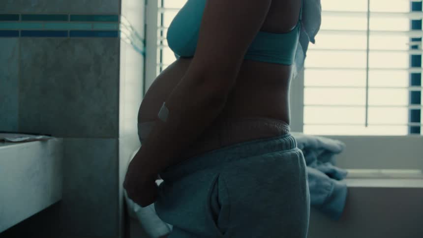 Pregnant woman tying her pants in the bathroom
