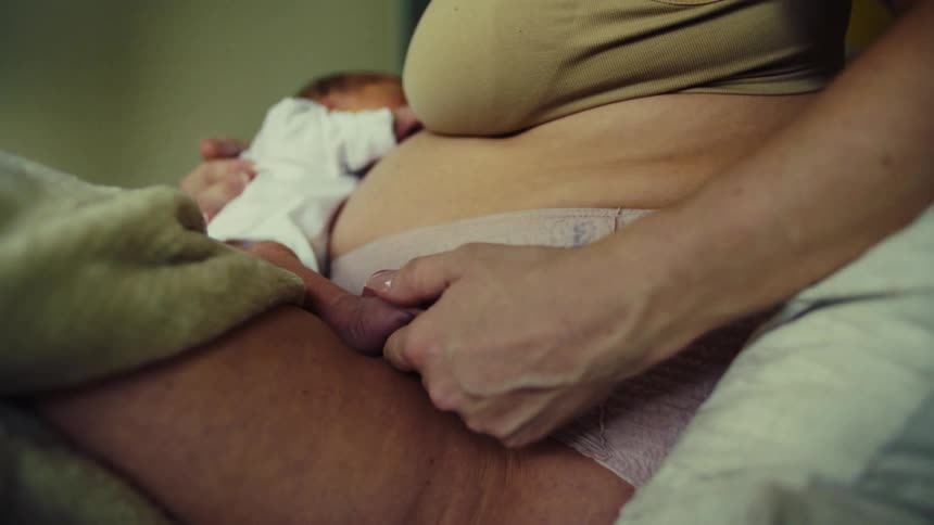 Mother sitting on bed stroking her newborn babys feet