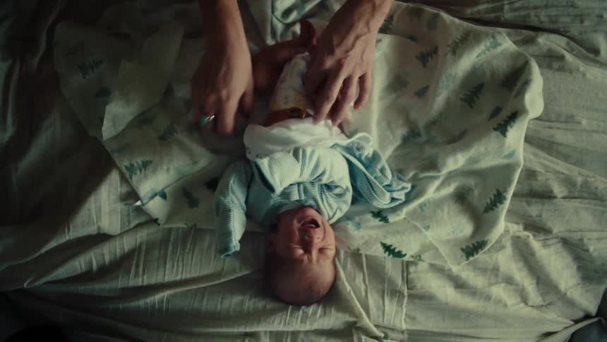 A person changing the diapers of a baby on a bed