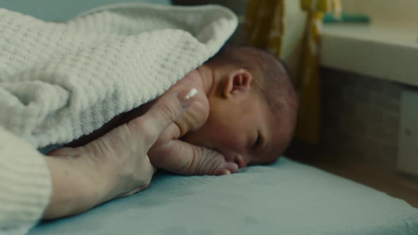 Hand carefully picking up a newborn baby who is lying on his stomach
