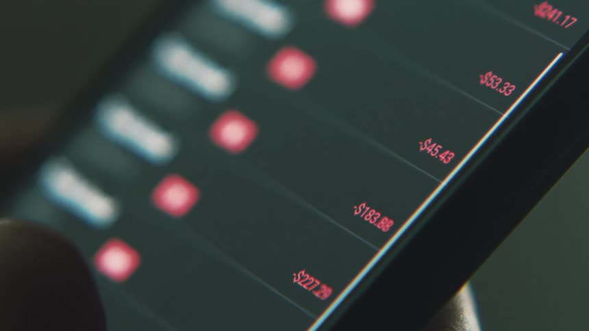 A thumb scrolls through stock prices on a smart phone app