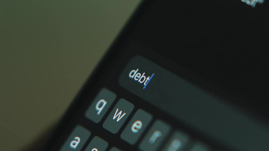 White letters are on a small keyboard as someone types debt