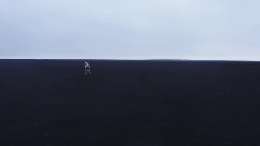 Person in white clothing walking on black ground on a cloudy day