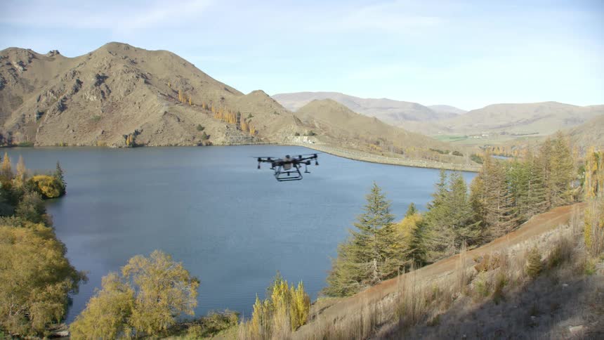 An industrial drone passes by a scenic lake and tall mountains