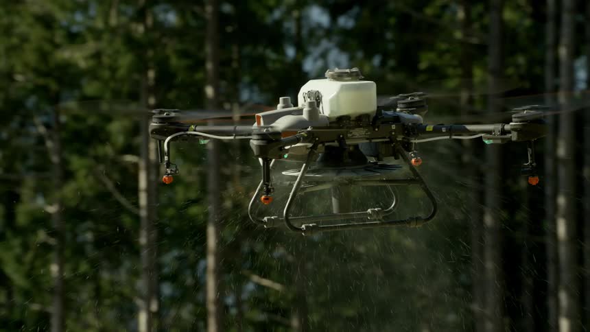 A drone in mid flight spraying liquid over a forest