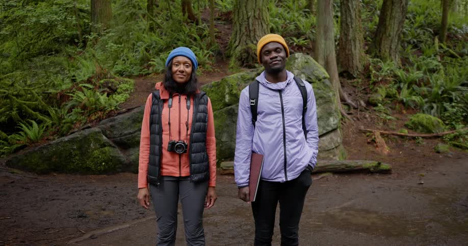 Man and woman side by side with one of them with a professional camera and the other holding a briefcase in a forest setting