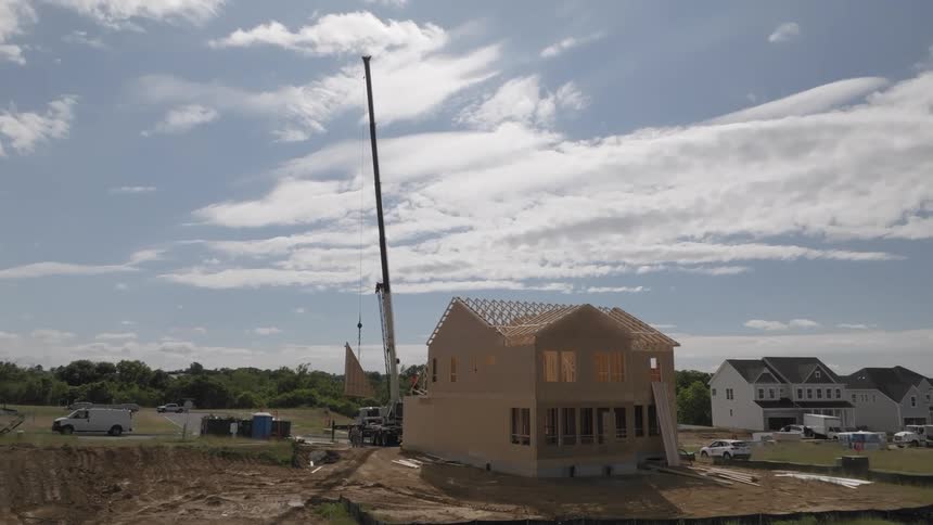 A crane lifting a wall to fit into a house under construction