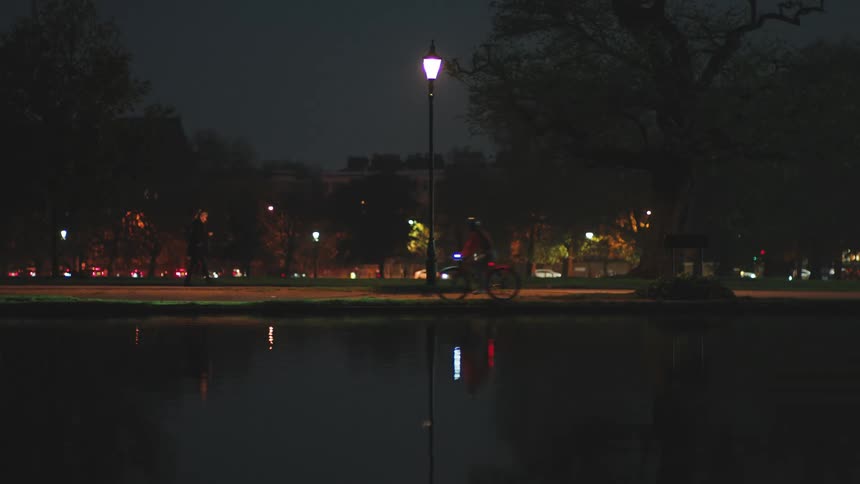 A lake reflecting the surrounding sidewalk landscape in a city at night