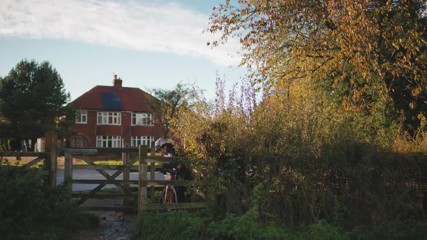 A young girl opens a gate and walks through it with her bicycle smiling