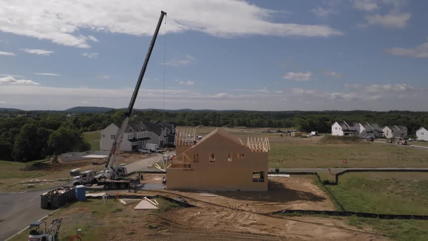 Construction crew works with a crane while building a house in a suburban neighborhood near the woods