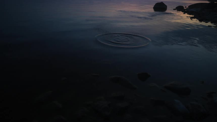 Small stone flying in a lake that reflects a sunrise
